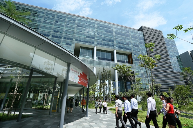 Group of people walking on a paved path beside a modern glass office building at MapleTree Business City